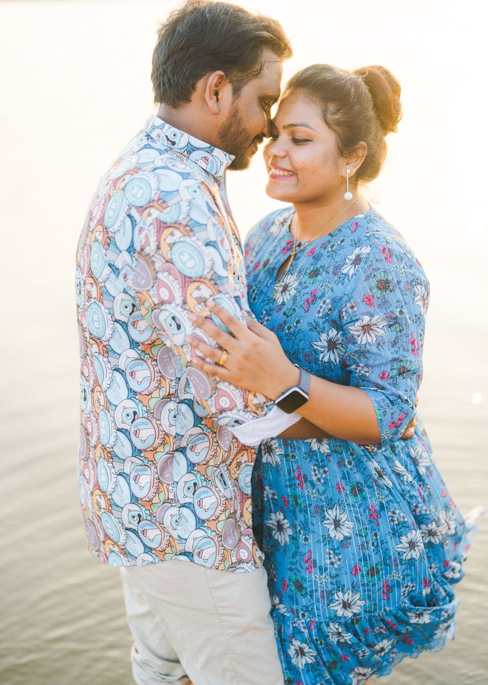 A couple in coordinating floral outfits sharing an intimate moment on a beach at sunset.