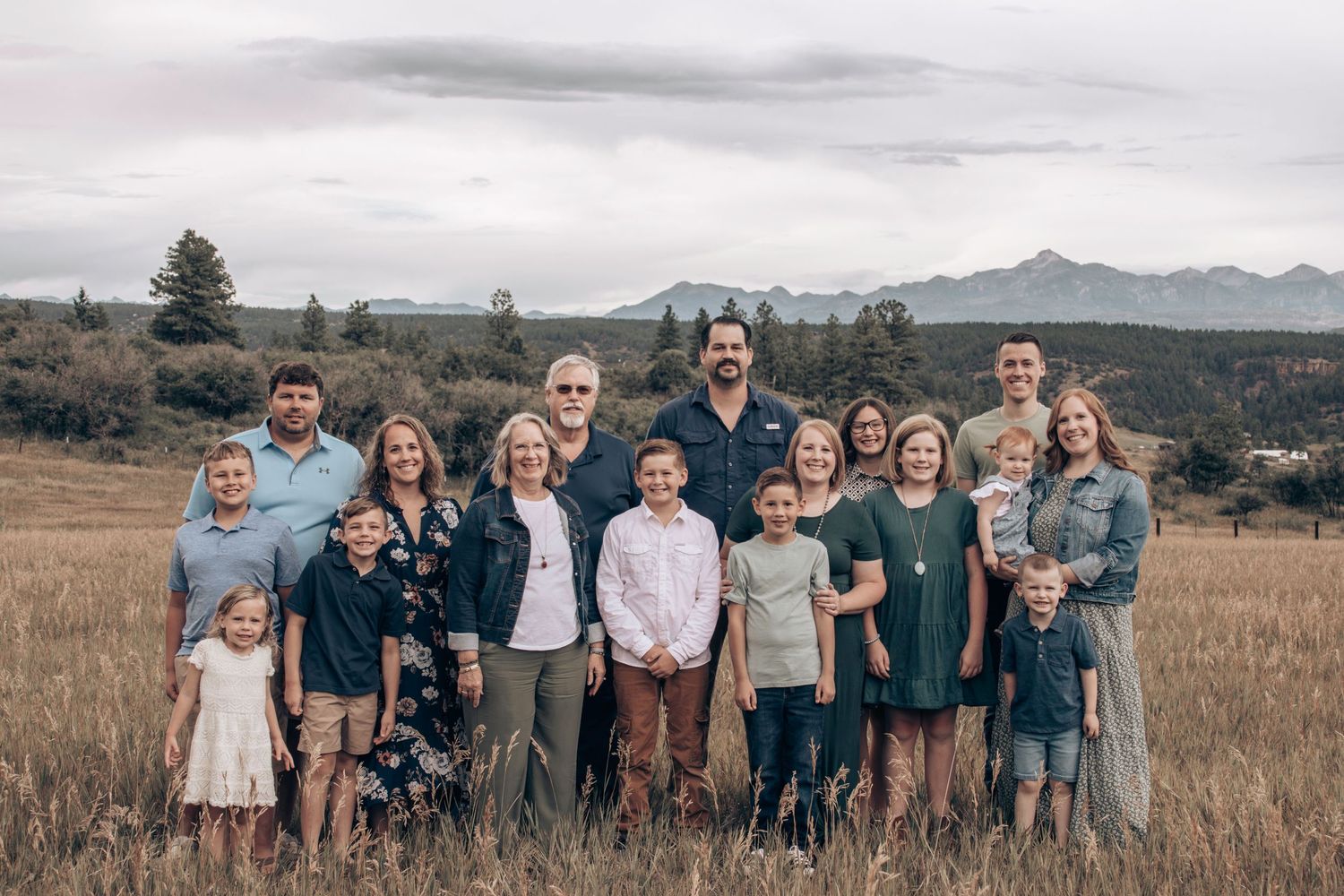 Extended family gathered for outdoor portrait session in mountain field setting.