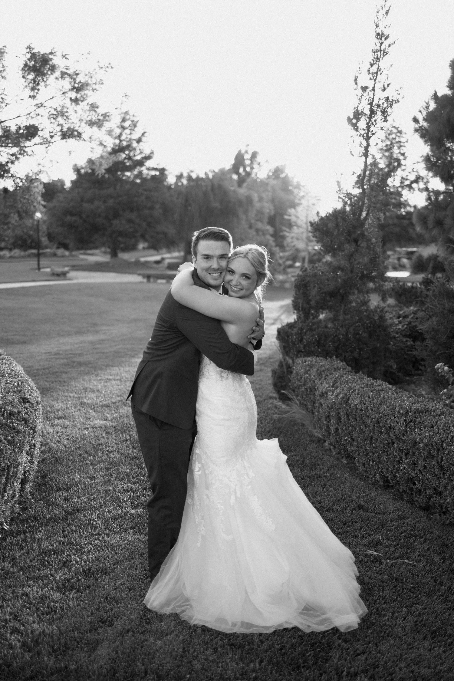 A romantic black and white wedding photo showing a couple embracing outdoors on a scenic lawn.