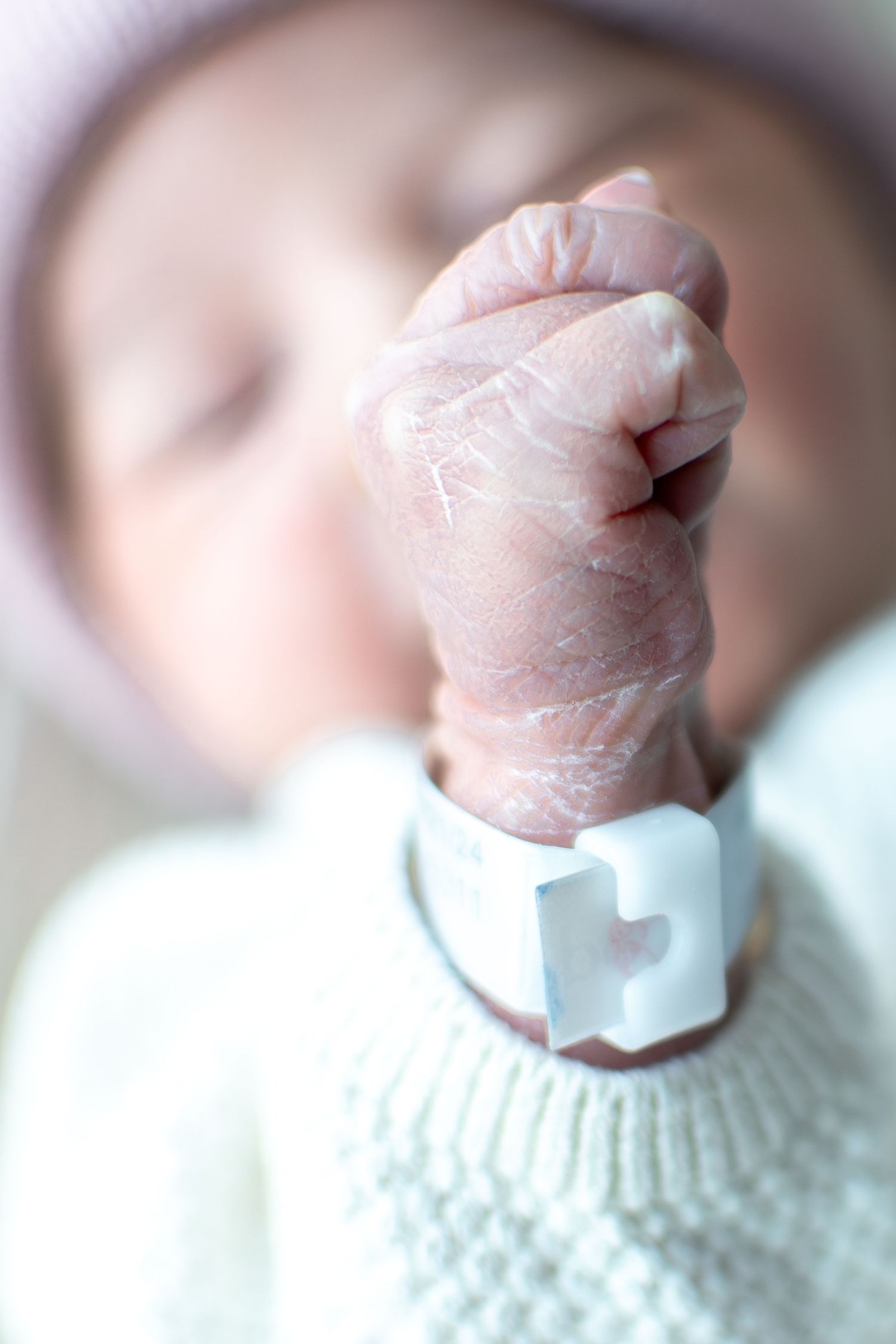 Close-up of tiny newborn baby's fist in white knit sweater.