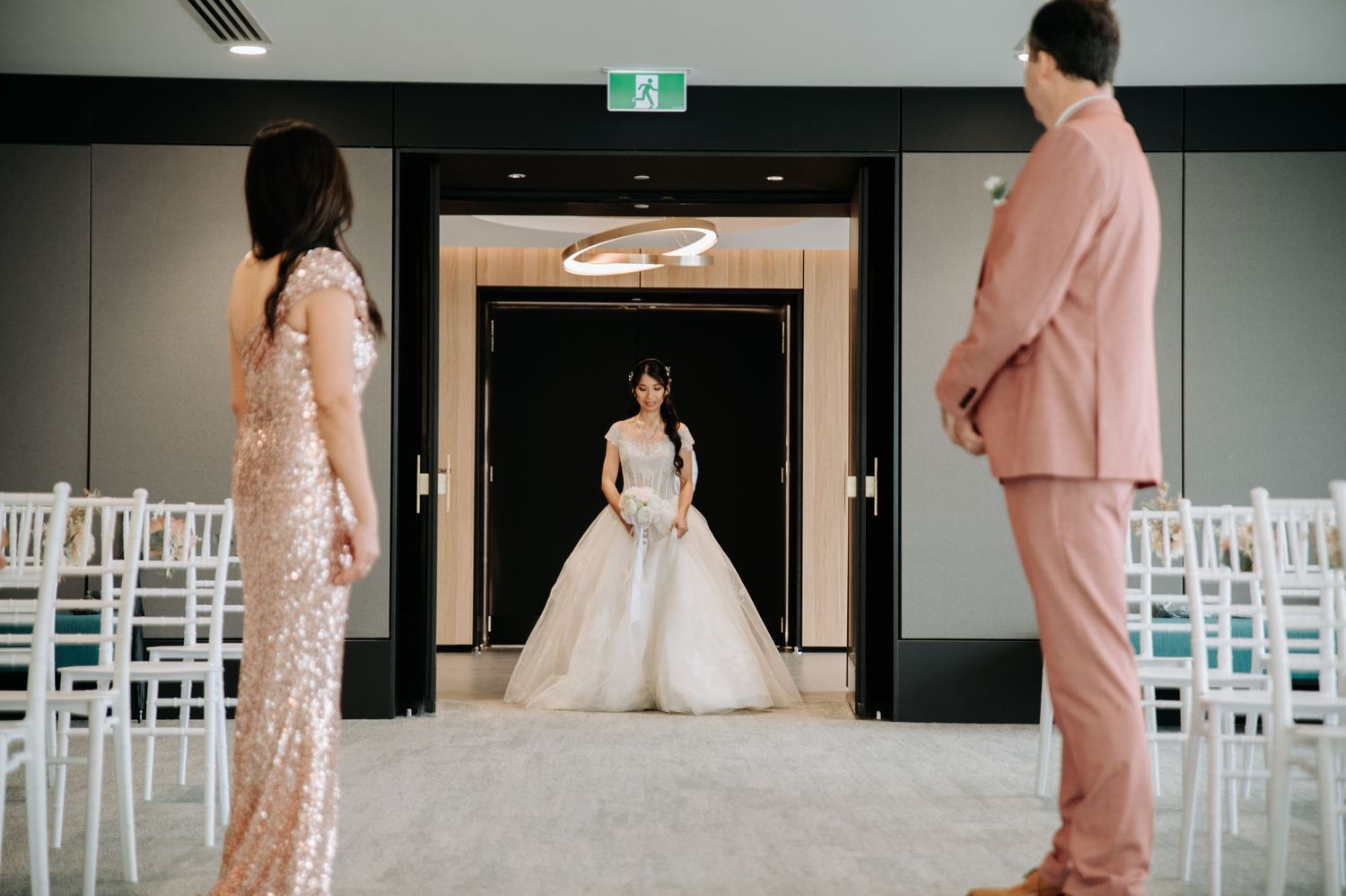 Wedding ceremony setup with white chairs and figures in formal attire.
