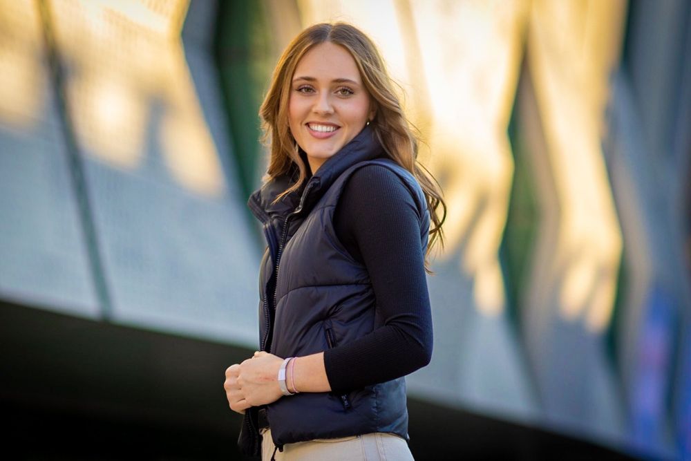 A person wearing a navy blue jacket smiles while standing outdoors during golden hour lighting.