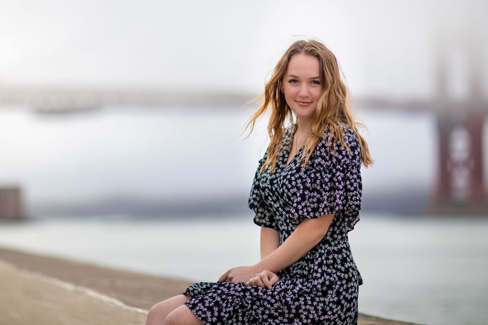 Woman in polka dot dress poses by Golden Gate Bridge on foggy San Francisco day.