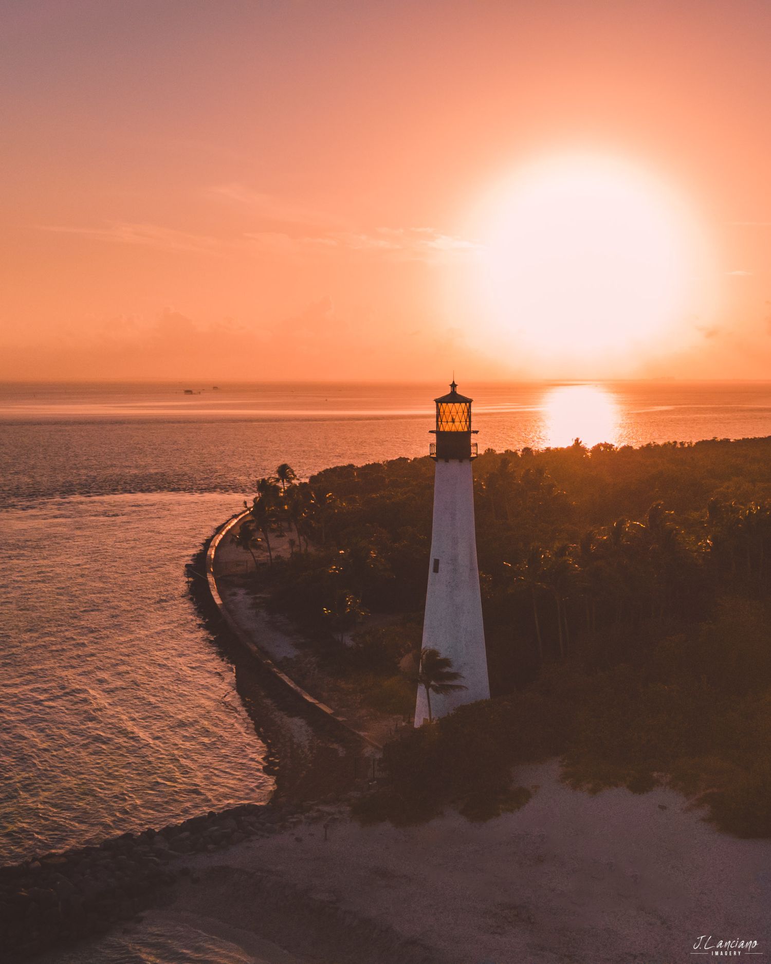 Lighthouse silhouetted against a dramatic orange sunset over coastal waters.