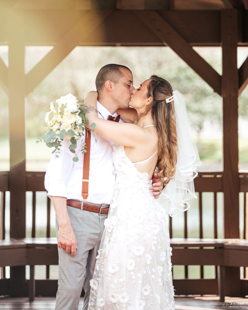 Romantic wedding moment captured under rustic wooden gazebo with floral bouquet.