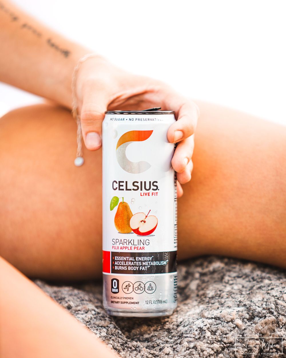 Celsius energy drink can in Fuji Apple flavor held against sunny background.