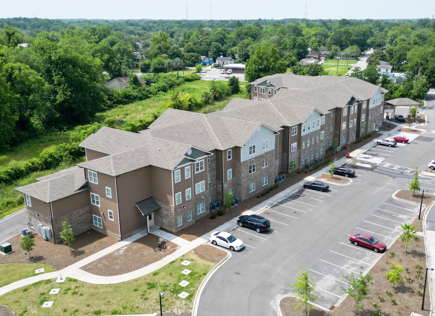 Aerial view of multi-unit townhouse complex with parking lot surrounded by trees.