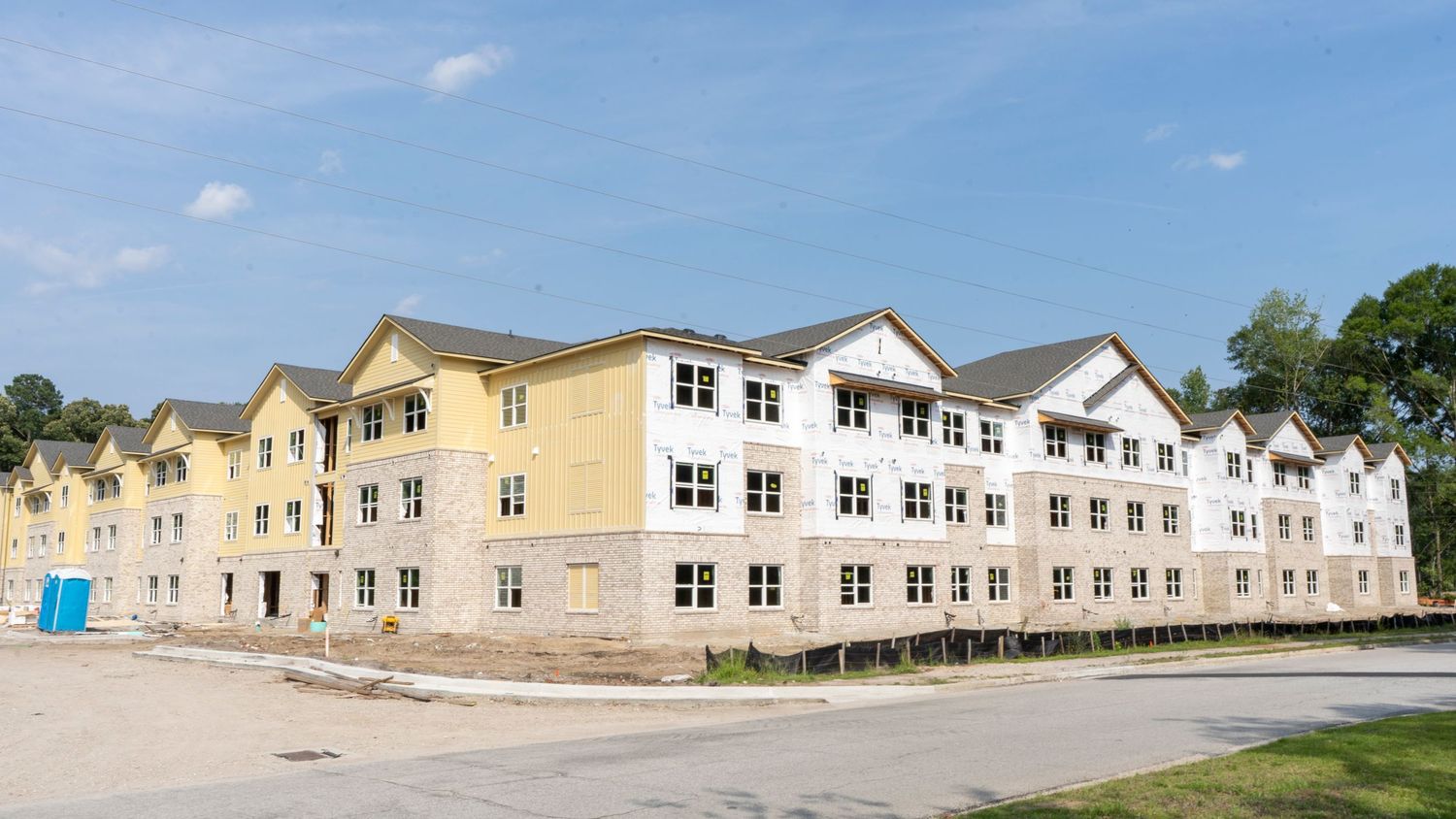 Yellow and white multi-story apartment complex under construction with parking area.