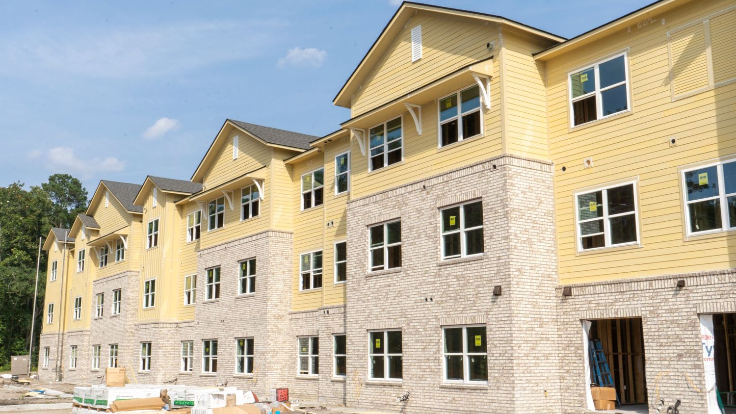 Modern apartment building exterior featuring yellow siding and stone accents during construction.