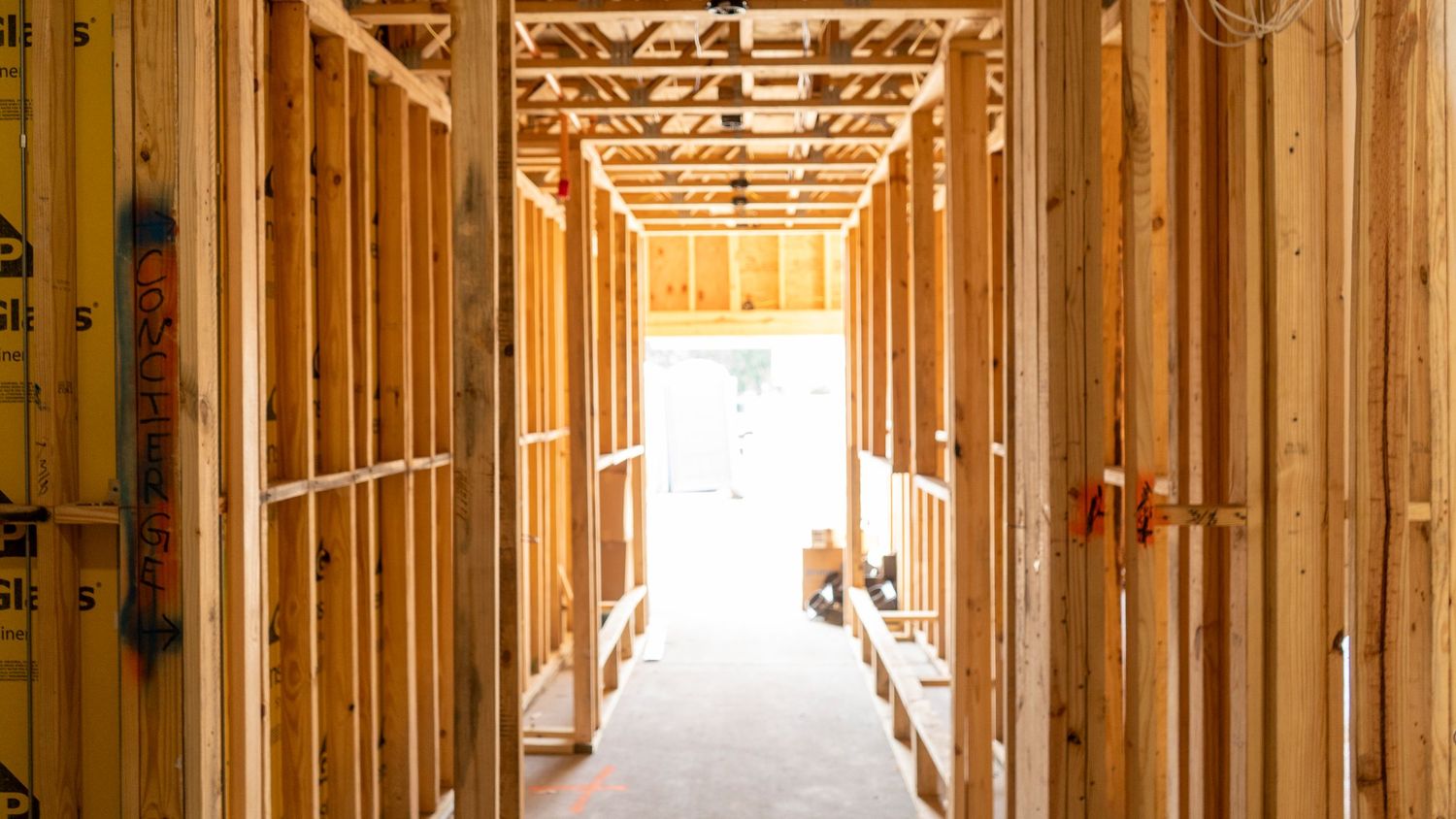 Interior framing of new construction showing wooden studs and ceiling trusses lit from end.