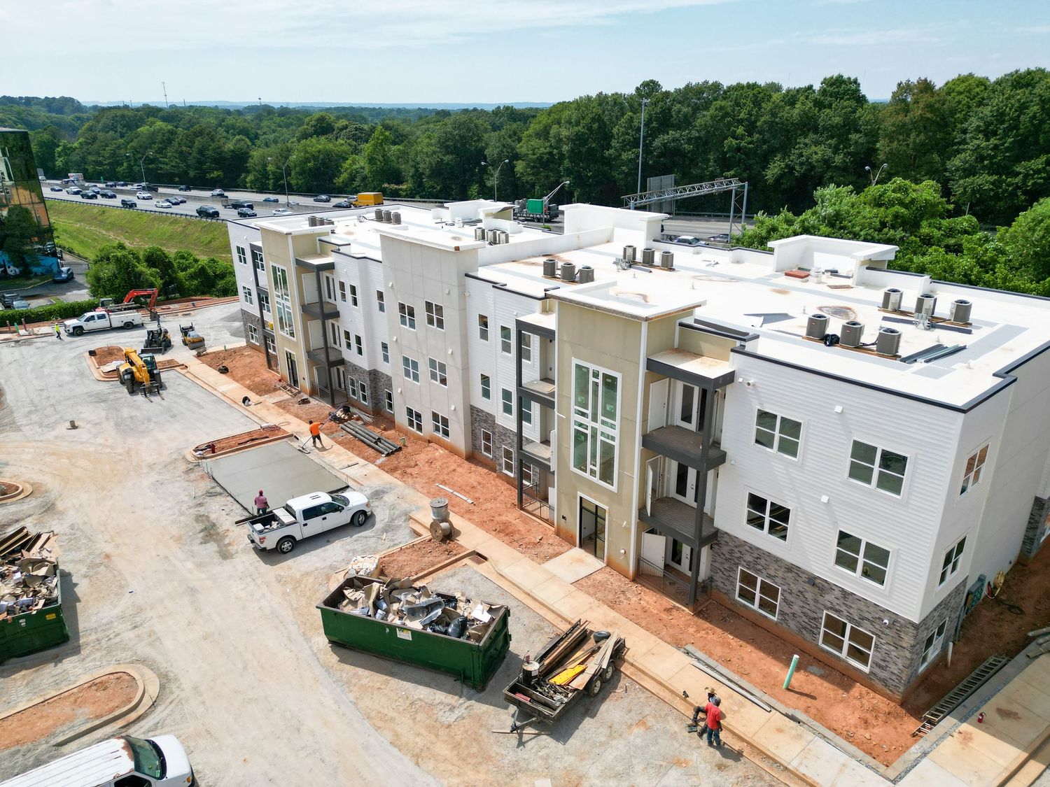 Modern apartment complex under construction with dumpsters and construction vehicles in foreground.