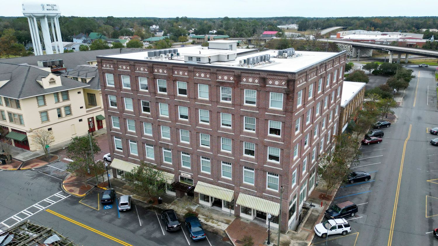 Historic red brick building with multiple stories in downtown setting with parked cars.