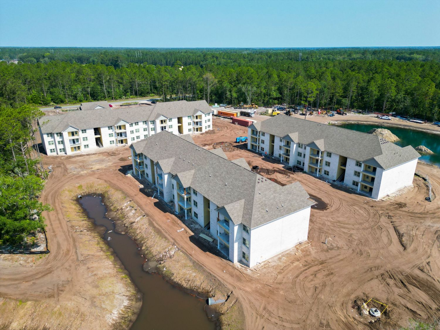 Bird's eye view of white apartment buildings under construction near wooded area.