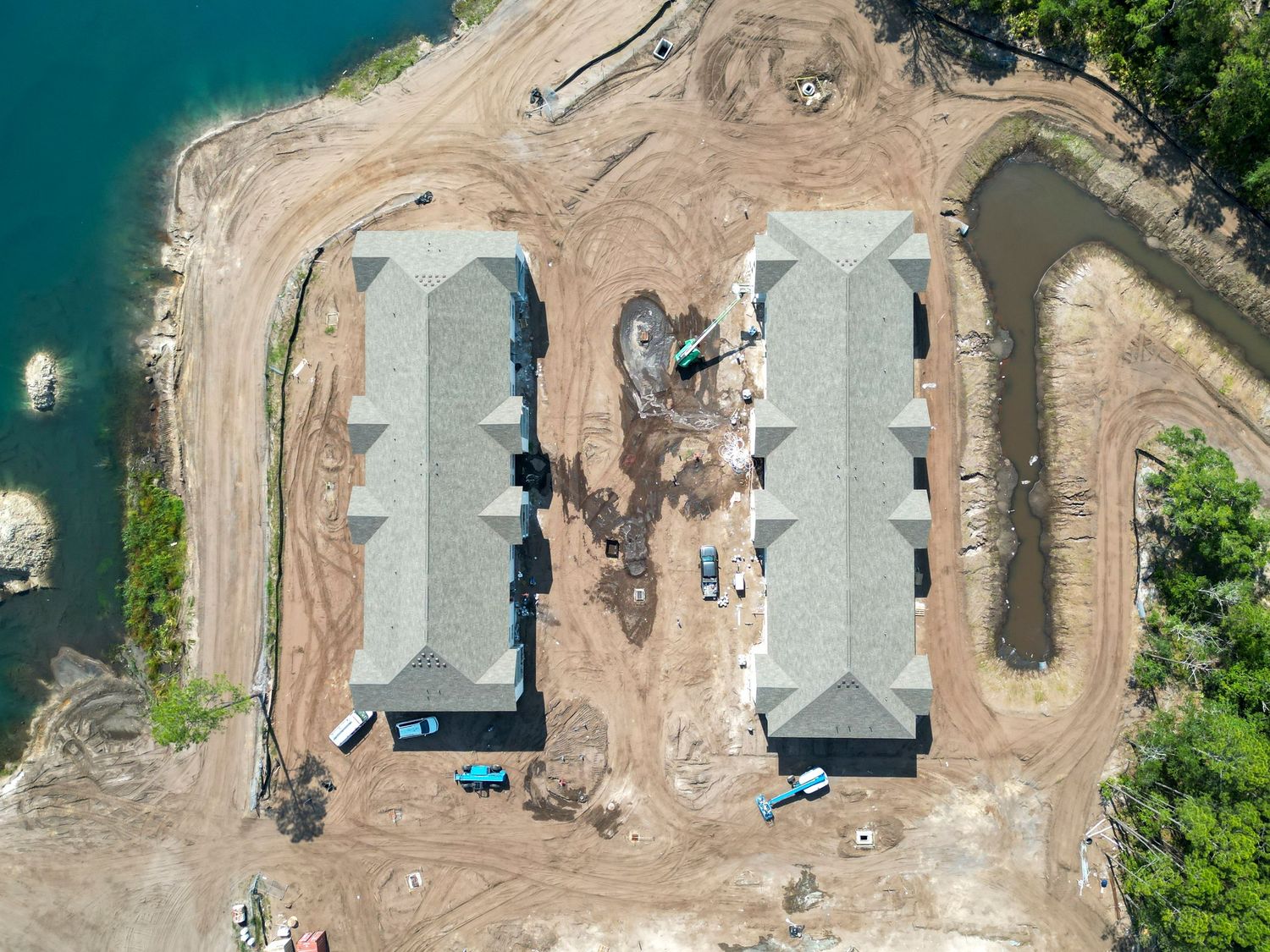 Top-down drone shot of two parallel apartment buildings under construction near waterfront.