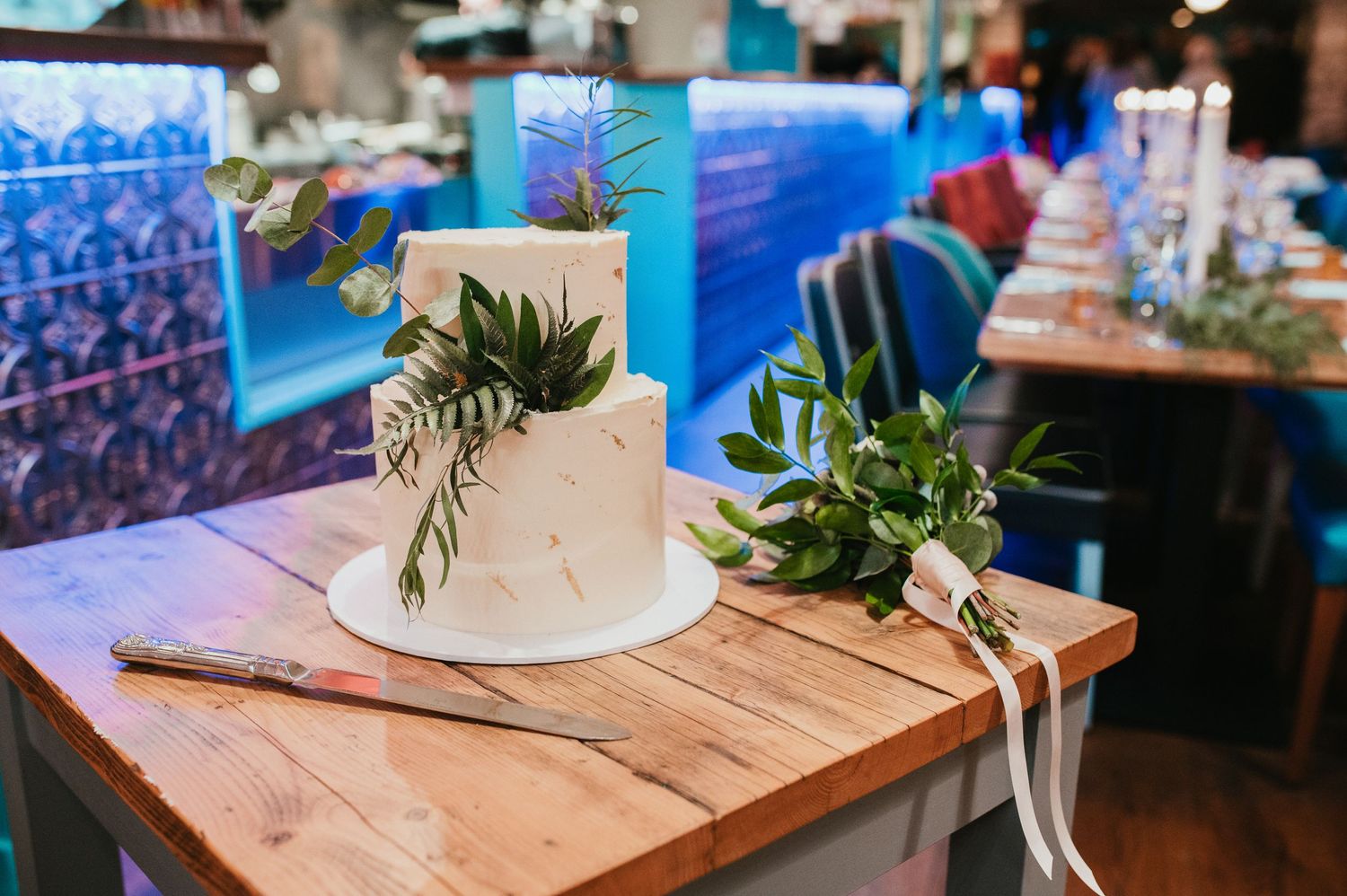 Elegant white wedding cake decorated with fresh greenery on wooden table.