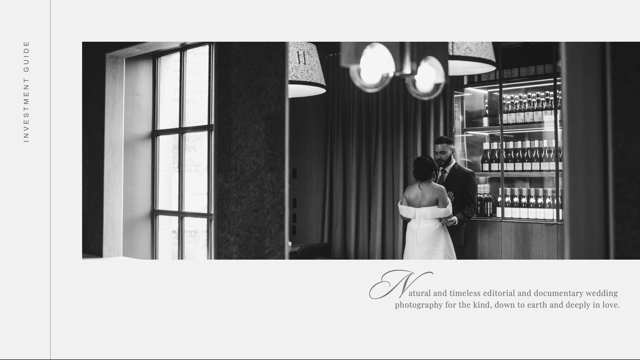 Elegant black and white wedding photo of bride and groom standing near large windows in a stylish venue.