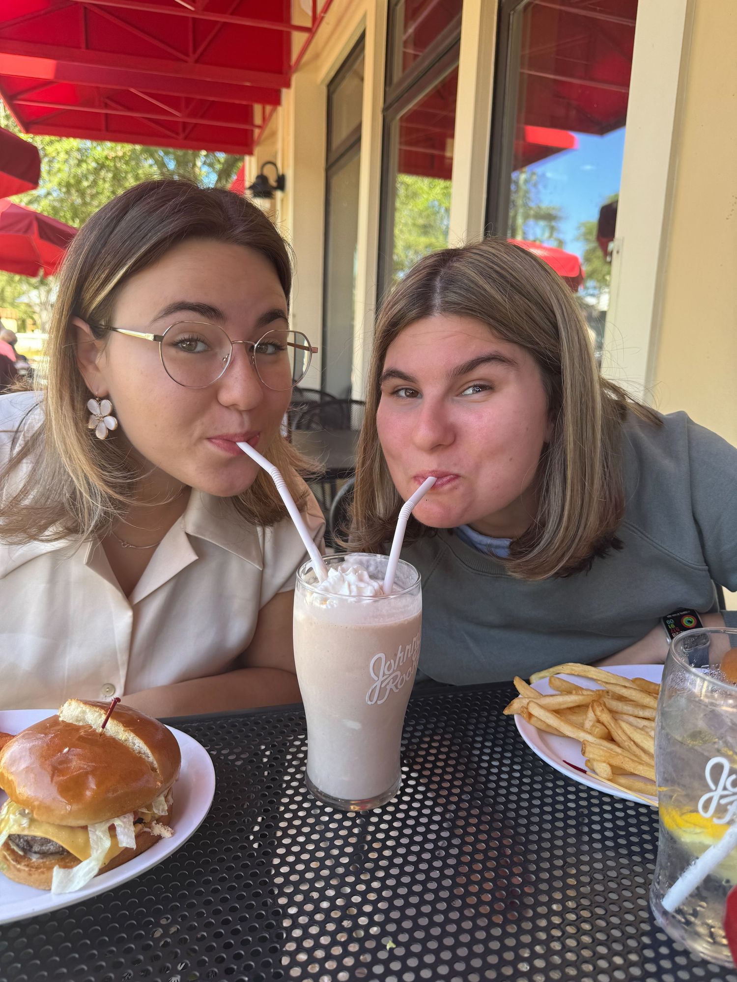 Friends enjoying burgers and milkshakes at an outdoor restaurant patio.
