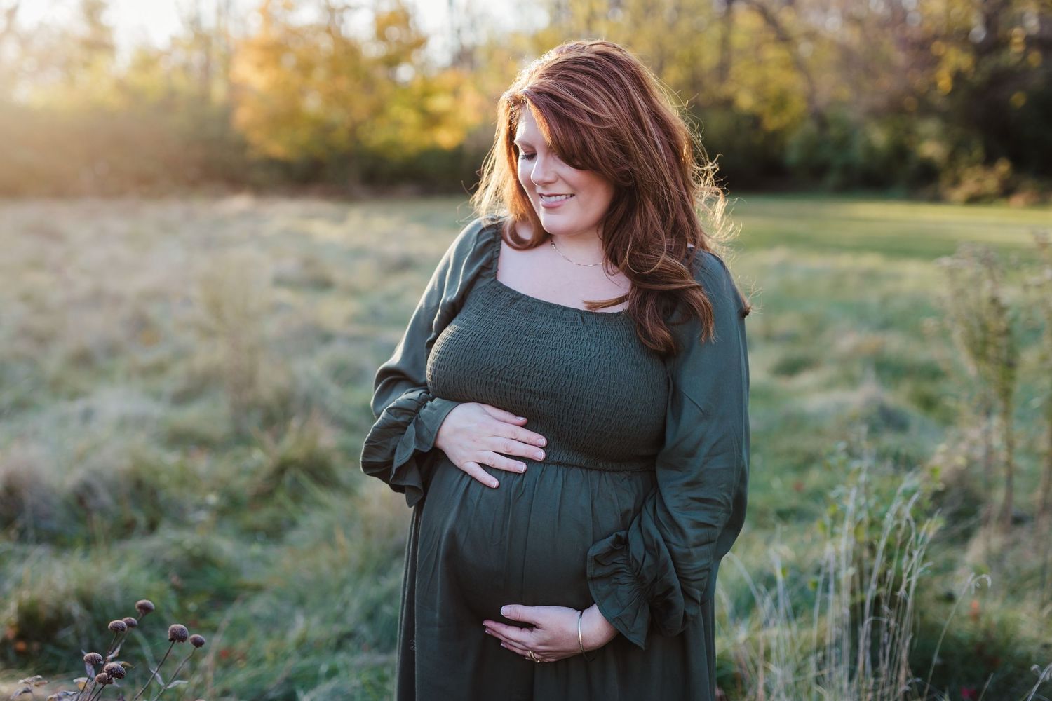 Expecting mother in red dress holding flowers during sunset in garden.