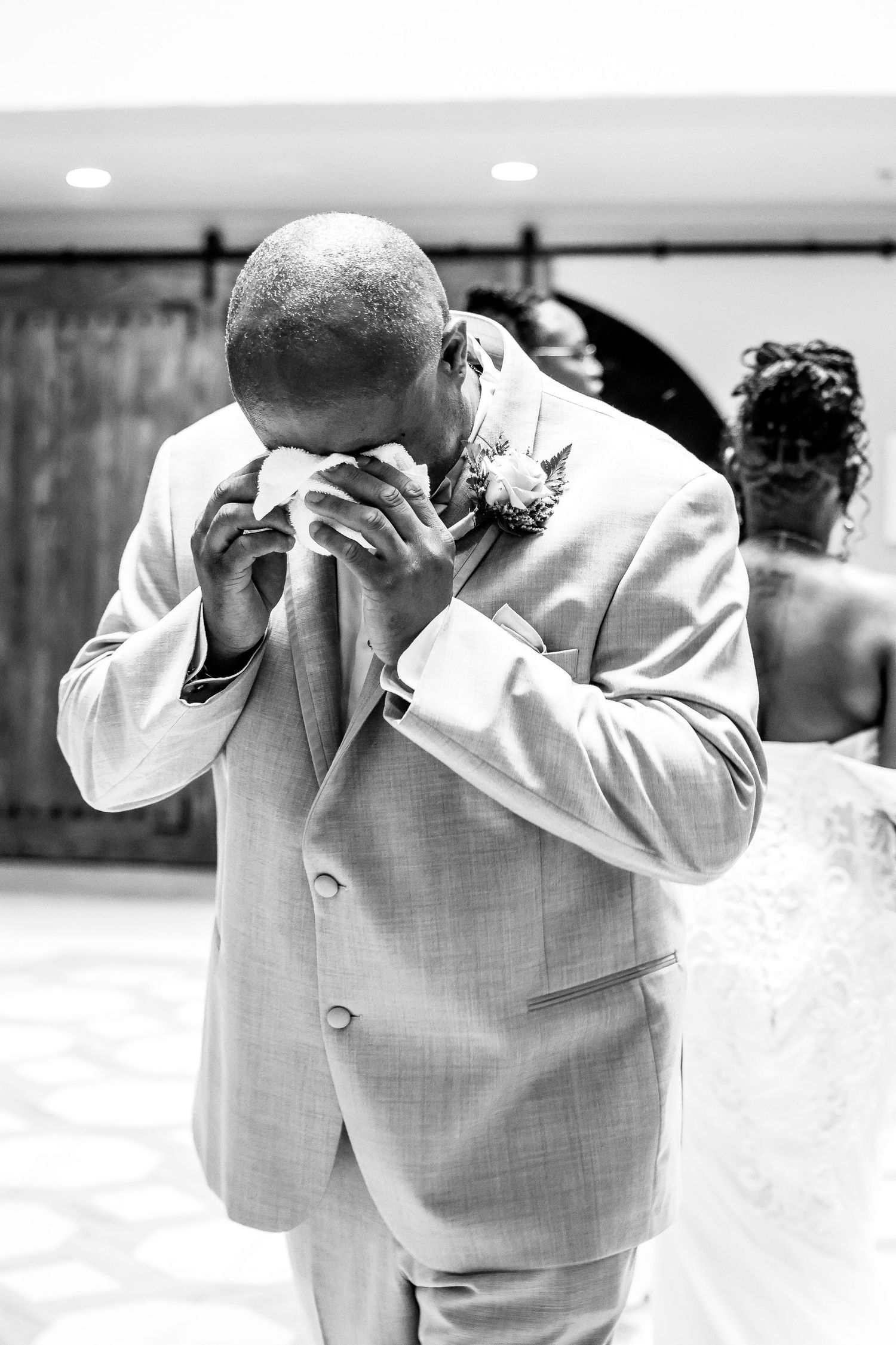 An emotional moment captured in black and white as a groom in light suit wipes away tears.