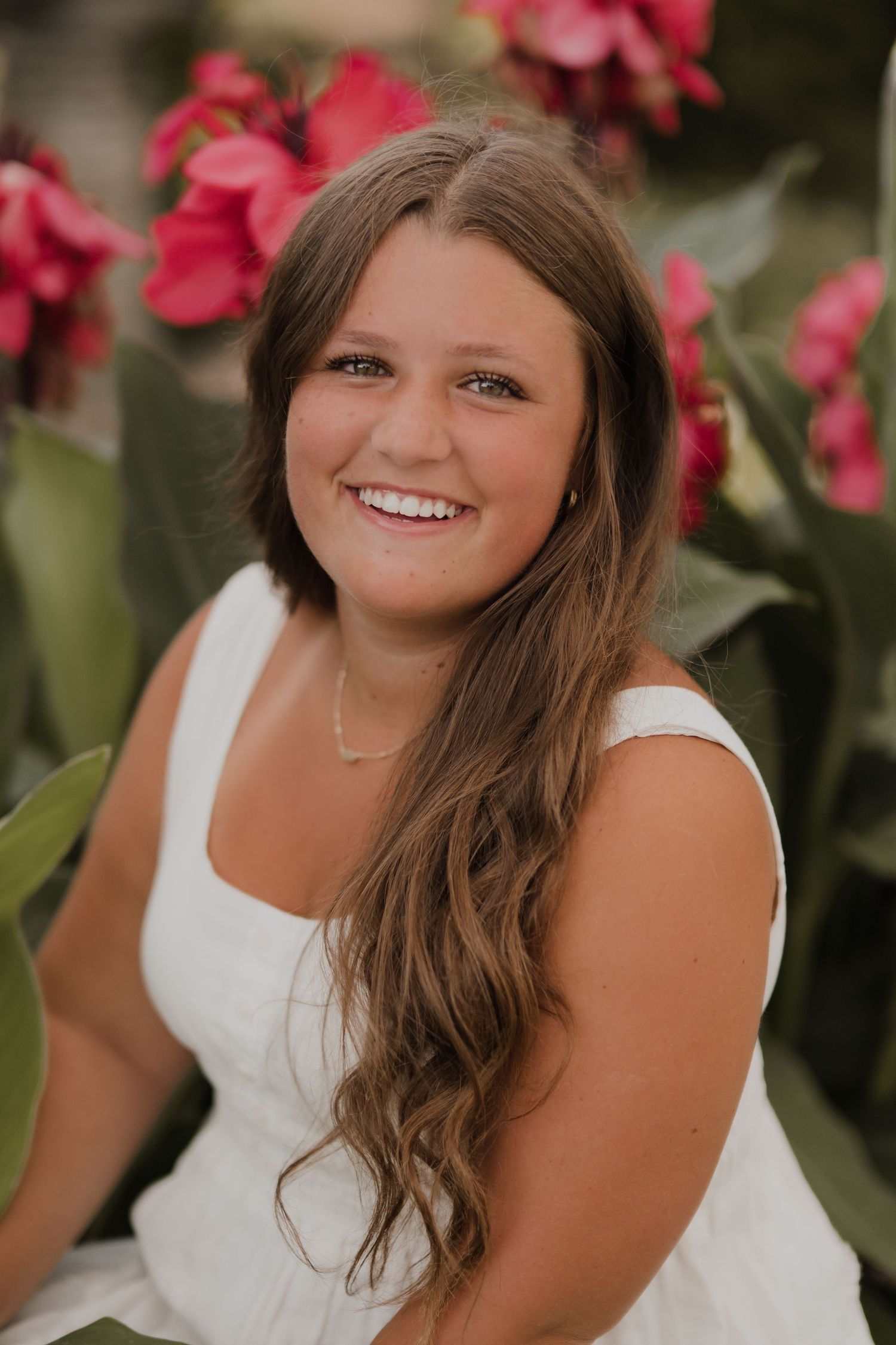 Person in white dress smiling against background of bright pink flowers.