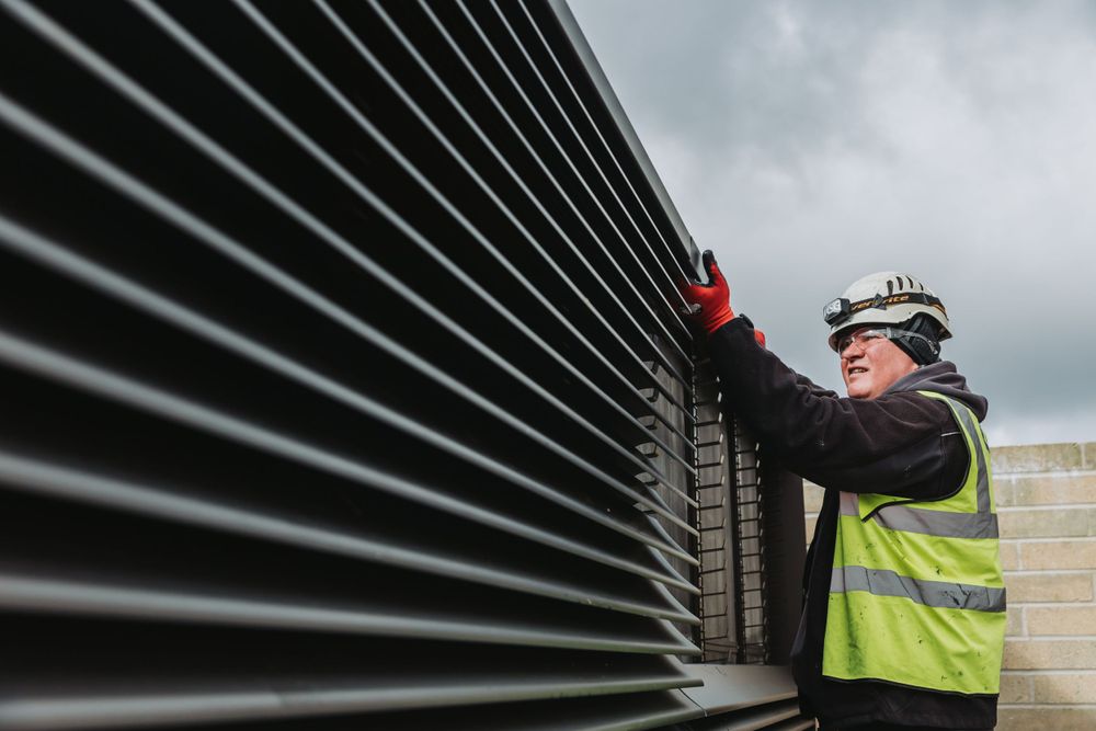 Industrial ventilation system with parallel metal slats being inspected outdoors.