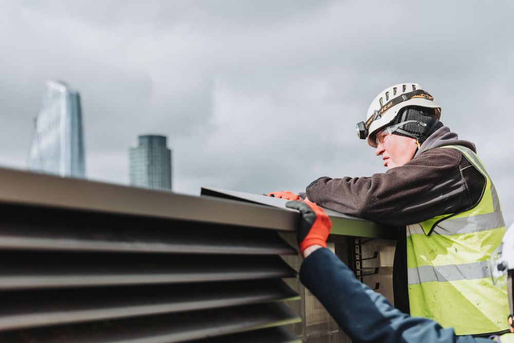 Worker in safety vest examining large industrial ventilation system components.
