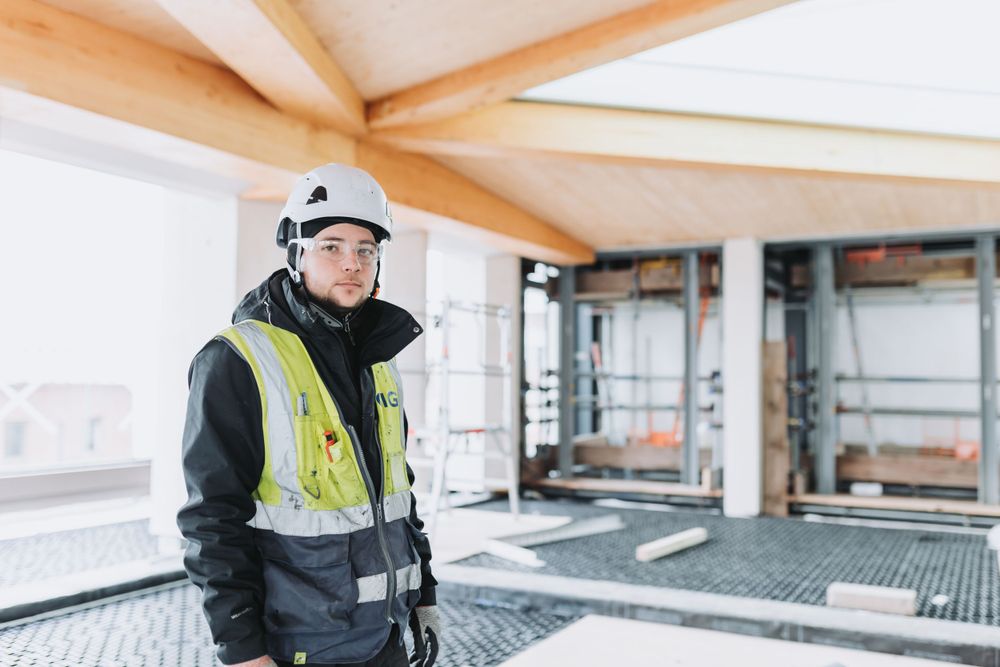 Construction worker in safety gear examines wooden beams on a building site.