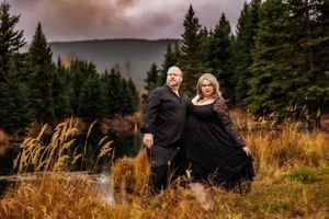 Couple in matching black attire stand together in front of scenic mountain vista with golden grass.