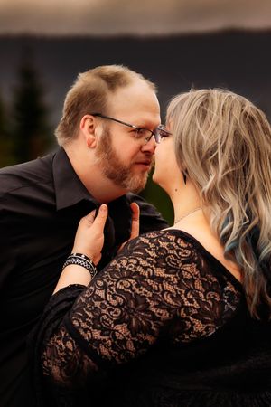 Intimate moment captured between couple in black attire against mountain landscape at dusk.