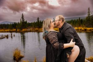 Intimate embrace captured on wooden dock with dramatic mountain landscape and autumn colors.