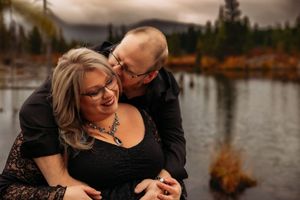 Joyful couple shares tender moment by mountain lake during sunset photo session.