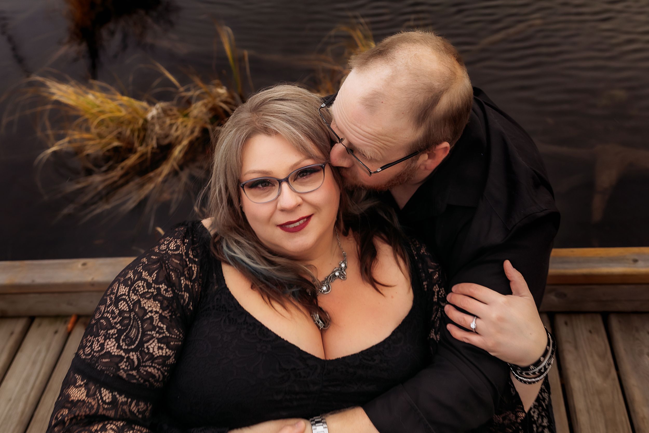 Couple shares intimate moment on wooden dock with dramatic autumn scenery.