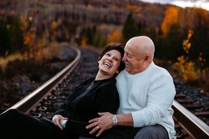 Two people share joyful laughter while sitting near train tracks during sunset.