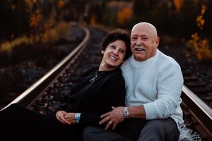 A couple shares candid moments of laughter while sitting on railroad tracks at dusk.