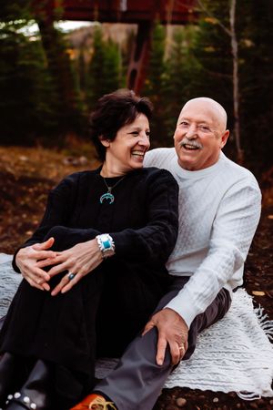 A couple laughs together while sitting on a white blanket during an autumn photo session.