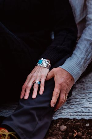 Close-up detail shot of hands with turquoise jewelry resting on a white lace blanket.