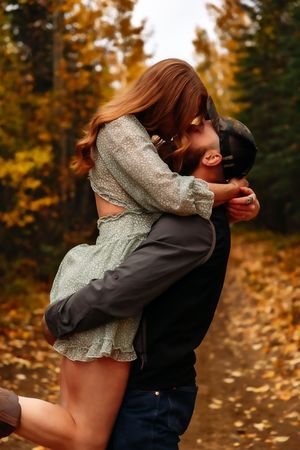 Couple shares joyful embrace on autumn path surrounded by golden foliage.
