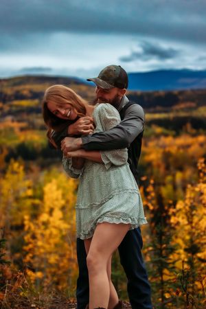 A romantic couple embraces in a dramatic dip pose against a backdrop of autumn foliage and mountain scenery.