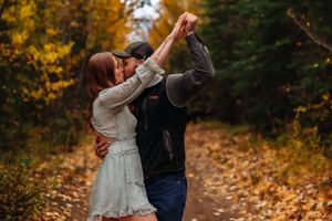 Couple dances together on leaf-covered forest path during fall.