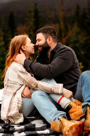 Intimate portrait of couple sharing loving moment on plaid blanket in mountains.