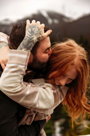 Candid shot of couple embracing with mountain vista and evergreens in background.
