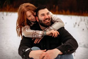Couple shares playful moment while sitting together in snowy setting.