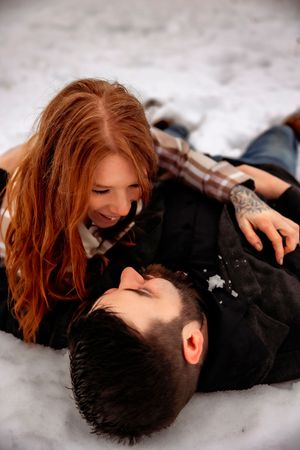 Couple shares intimate moment lying in snow during winter photoshoot.