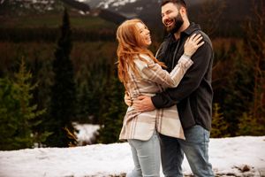 Couple shares romantic embrace against mountain backdrop with snow covered peaks.