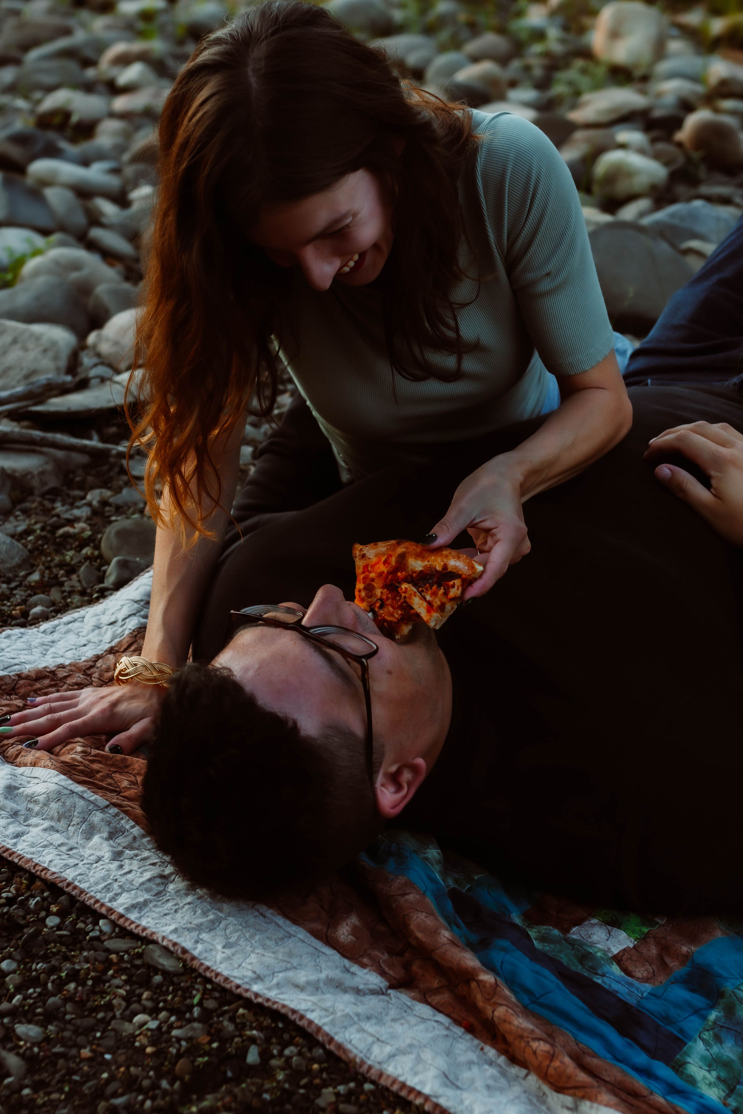 Couple sharing intimate moment on rocky riverbank during sunset.