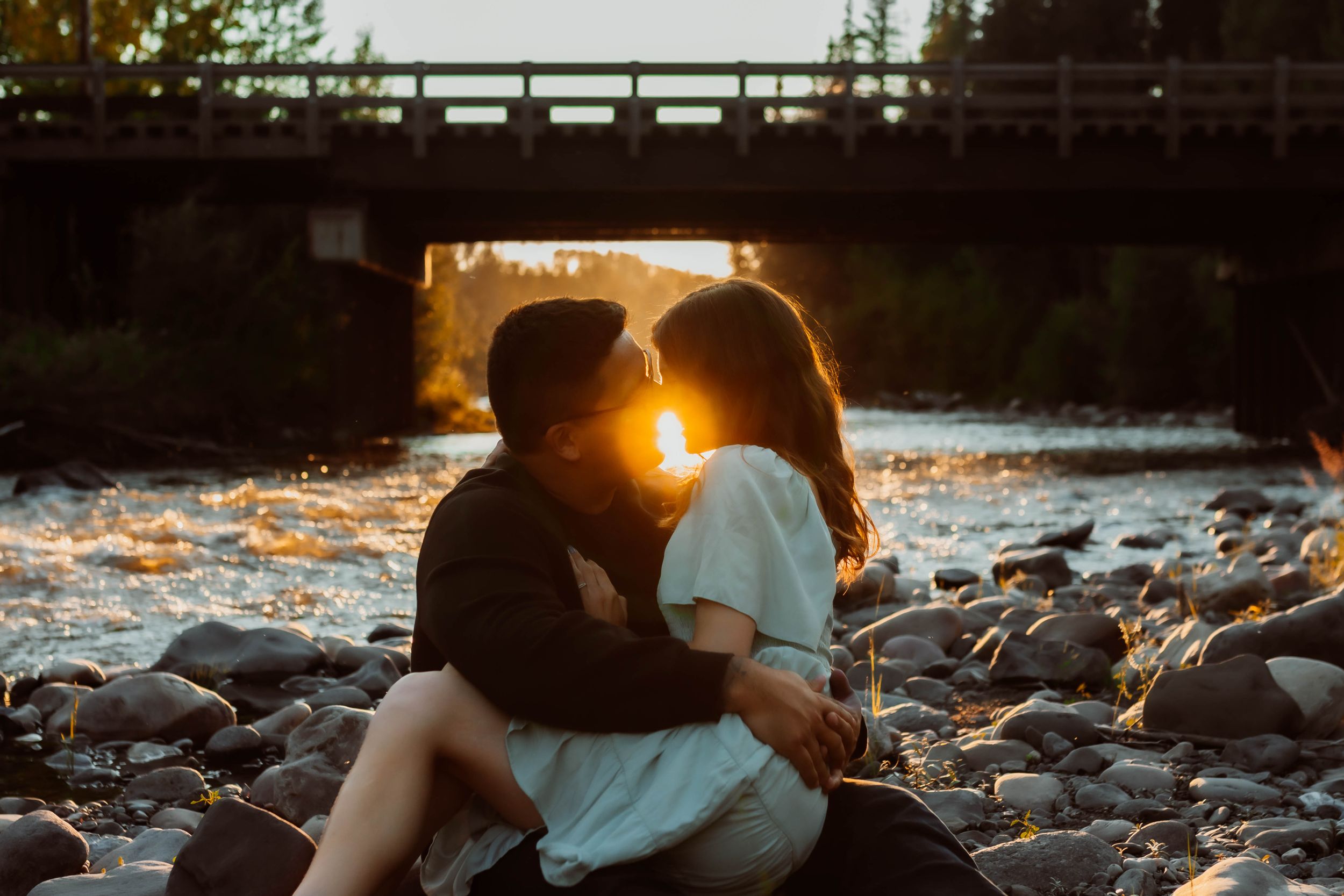 Silhouetted couple sharing tender moment by bridge during sunset.