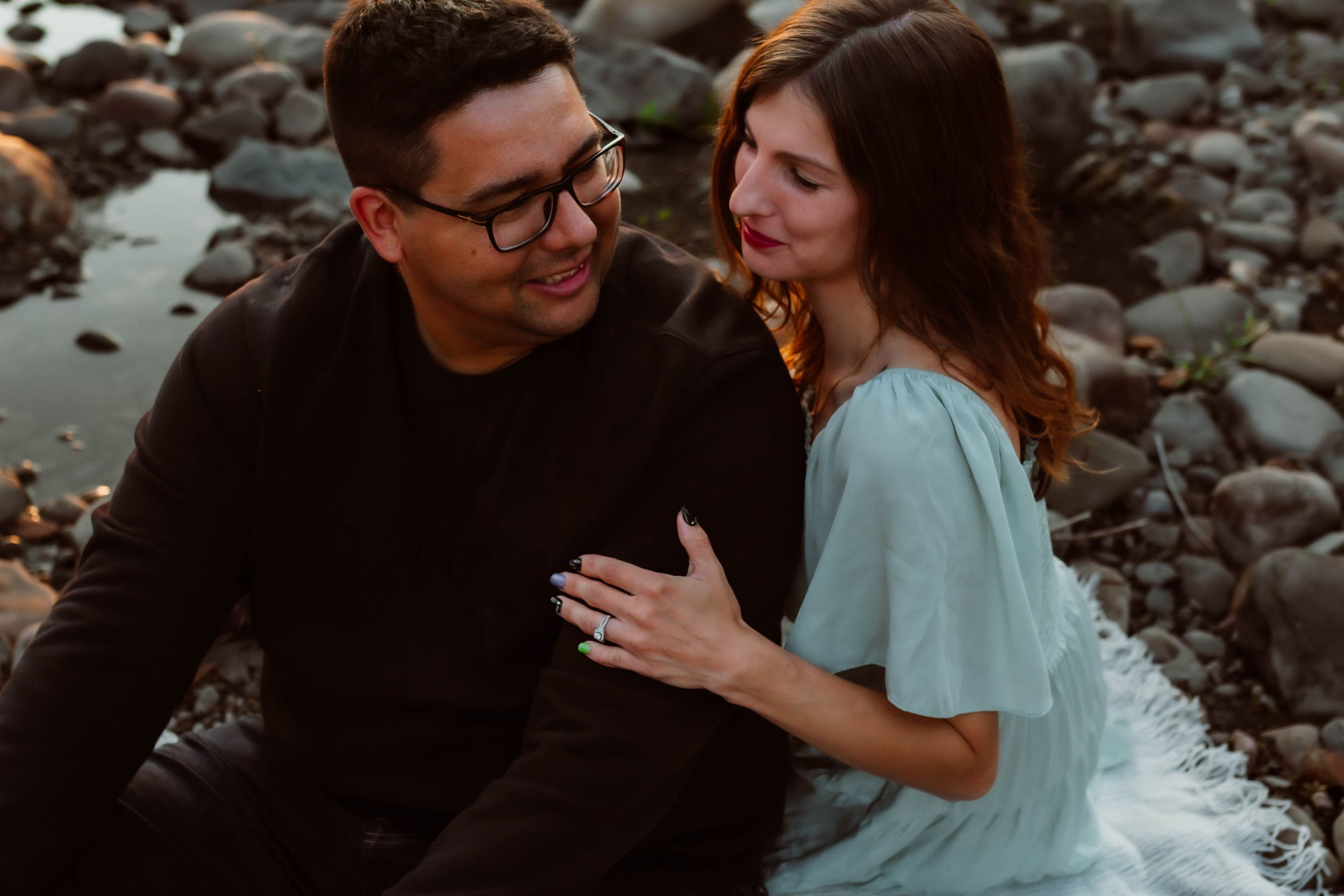 Couple shares an intimate moment while sitting on rocky shore during golden hour sunset.