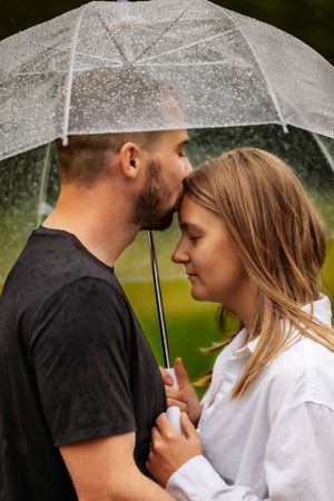 Romantic couple shares intimate moment under clear umbrella in the rain.