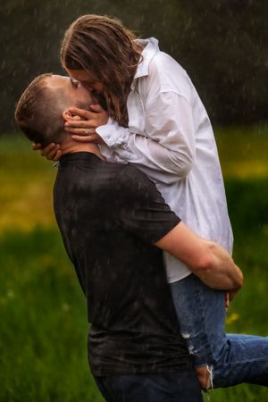 Romantic couple sharing passionate embrace in rain-soaked field.