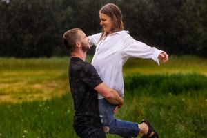 Couple shares joyful moment in the rain as they embrace in a grassy field.